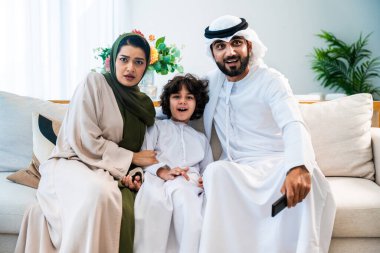 Geleneksel emirati kıyafetleri giyen Ortadoğu ailesi evde birlikte vakit geçiriyorlar. Arap ailesi kanepede televizyon seyrediyor, şaşırmış ve endişeli ifadeler sergiliyorlar.
