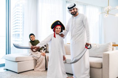 Geleneksel emirati kıyafetleri giyen Ortadoğu ailesi evde birlikte vakit geçiriyorlar. Orta Doğulu aile, modern oturma odalarında birlikte oynuyorlar.