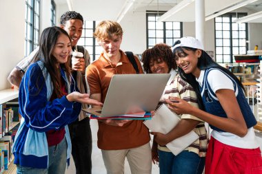 Çok ırklı bir grup genç öğrenci kütüphanede buluşuyor. Çeşitli kolej öğrencileri gülümsüyor, dizüstü bilgisayarda birlikte çalışıyorlar. Modern bir üniversite kütüphanesinde duruyorlar.