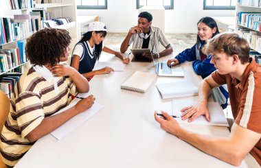 Çok ırklı bir grup genç öğrenci kütüphanede toplanıyor. Modern bir kütüphane ortamında bir proje üzerinde çalışan, öğrenen ve araştırma yapan çok ırklı bir grup genç üniversite öğrencisi.