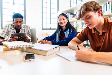 Kütüphanede bir araya gelen çok ırklı genç öğrenci grubu - kütüphanede üniversite projesinde işbirliği yapan, bilgiyi paylaşan ve dijital araçları öğrenmek için kullanan çok ırklı genç öğrenciler.
