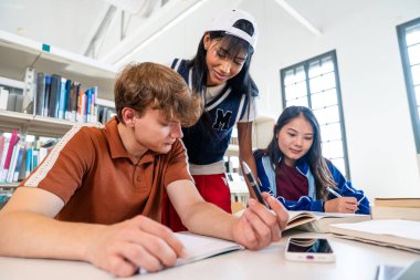 Kütüphanede toplanan çok ırklı bir grup genç öğrenci. Üniversite kütüphanesinde işbirliği yapan ve öğrenen çok ırklı genç öğrenciler. Eğitimleri için kitap ve teknoloji kullanıyorlar.