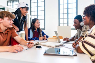 Kütüphanede bir araya gelen çok ırklı genç öğrenci grubu. Laptoplar ve kitaplar kullanarak, akademik başarı ve takım çalışması fikirlerini paylaşarak birlikte çalışan çeşitli genç öğrenciler.