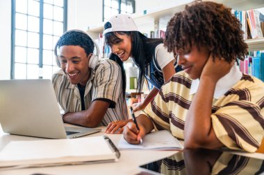 Kütüphanede toplanan çok ırklı bir grup genç öğrenci. Parlak bir kütüphanede bir proje üzerinde işbirliği yapan, gülümseyen, dizüstü bilgisayar kullanan ve notlar yazan genç öğrenciler.