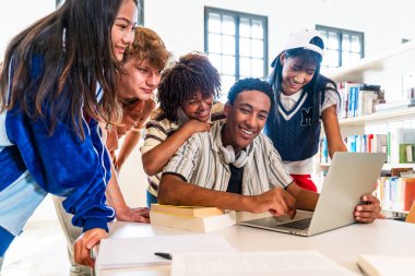 Multiethnic group of young students meeting at the library - multiethnic group of young students smiling, collaborating on a laptop computer while studying in a modern library