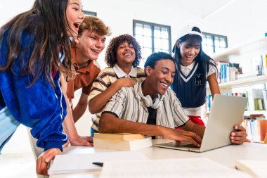 Multiethnic group of young students meeting at the library - diverse group of happy young students collaborating with laptop in a modern library. Sharing ideas in an educational environment