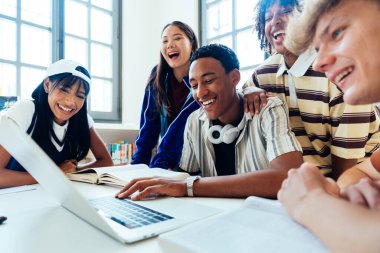 Kütüphanede buluşan çok ırklı bir grup genç öğrenci. Üniversite kütüphanesinde dizüstü bilgisayar ve kitapları kullanarak gülümseyen ve gülen bir grup genç öğrenci.