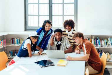 Kütüphanede buluşan çok ırklı bir grup genç öğrenci. Dizüstü bilgisayar ve kitaplarla aydınlık bir kütüphane masasında birlikte çalışan çok ırklı bir grup.