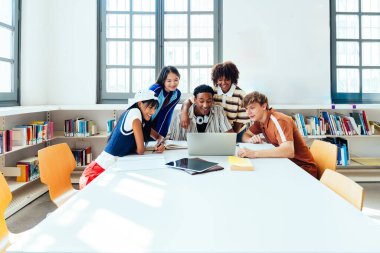 Kütüphanede buluşan çok ırklı bir grup genç öğrenci, bir okul kütüphanesinde dizüstü bilgisayarın etrafında toplanarak, işbirlikçi öğrenim ve öğrenim ile aktif olarak ilgilendiler.