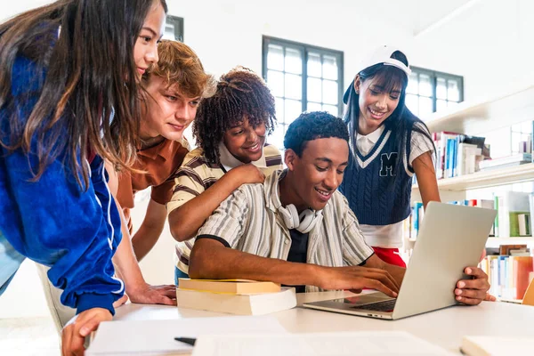 Çok ırklı bir grup genç öğrenci kütüphanede buluşuyor. Çeşitli öğrenciler birlikte gülümsüyor, dizüstü bilgisayarda çalışıyor ve modern bir okul kütüphanesinde okuyor.