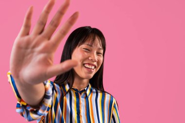 Renkli arka planda güzel bir Çinli kadın portresi. Genç Asyalı kadın elleriyle mutlu bir şekilde dur işareti yapıyor. Canlı pembe bir stüdyo arka planında portre fotoğrafı.