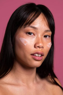 Renkli arka planda güzel bir Çinli kadın portresi. Asyalı kadının yakın plan doğal portresi, yüzüne nemlendirici sürerek canlı pembe bir stüdyo arka planına karşı