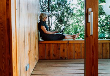 Üst düzey bir kadın sundurmada çalışıyor, yalın ayak ve rahat, huzurlu yeşil ağaçların tadını çıkarıyor uzaktan kumanda, esneklik ve dengeli bir açık hava yaşam tarzı..