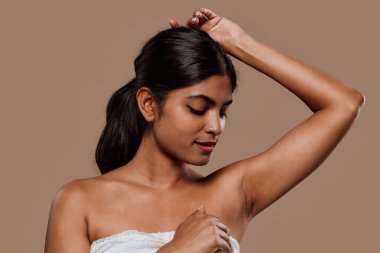 Profesyonel stüdyo portresi, uzun siyah saçlı, gerçek duygularını ifade eden, tarafsız kahverengi arka planda poz veren Hintli genç bir kadını çekiyor.