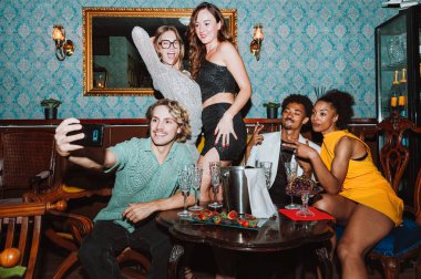 Çeşitli yetişkin arkadaşlar bir partide gülümsüyor ve selfie çekiyor. Şampanyayla ve abur cuburlarla özel bir kutlama yapıyorlar.