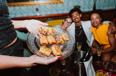 Arkadaşlar şampanya kadehlerini tokuştururken bir kadın şık bir barda, neşeli bir akşam kutlaması sırasında aperatifler sunuyor.