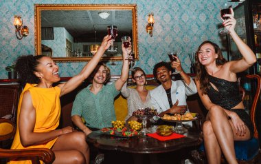 Çeşitli genç yetişkinler sosyal bir toplantının keyfini çıkarıyor, gülümsüyor, gülüyor ve bir bar veya restoran masasında ferahlatıcı içecekler ve aperatiflerle etkileşime geçiyorlar.