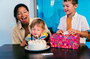 Asyalı bir aile evde. Asyalı bir anne ve iki çocuğu doğum gününü evde kutluyorlar. Kardeşim hediyesini açarken küçük çocuk pastaya mum üflüyor.