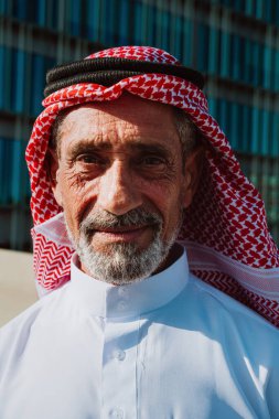 Geleneksel beyaz kandura ve ghutra içinde yaşlı Arap adam, bilgelik, miras ve kültürel gurur taşıyan açık hava portresi içinde güvenle gülümsüyor