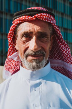 Geleneksel beyaz kandura ve ghutra içinde yaşlı Arap adam, bilgelik, miras ve kültürel gurur taşıyan açık hava portresi içinde güvenle gülümsüyor