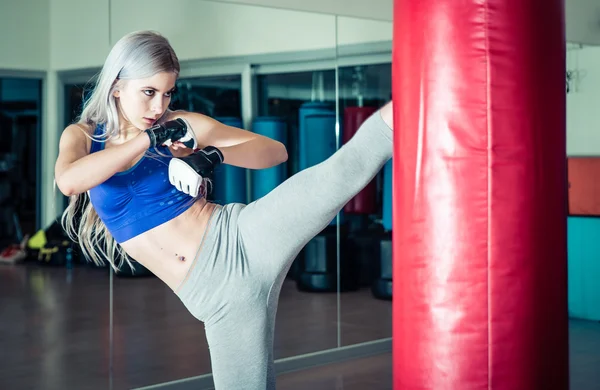 Woman hits the heavy bag with a strong kick — Stock Photo, Image