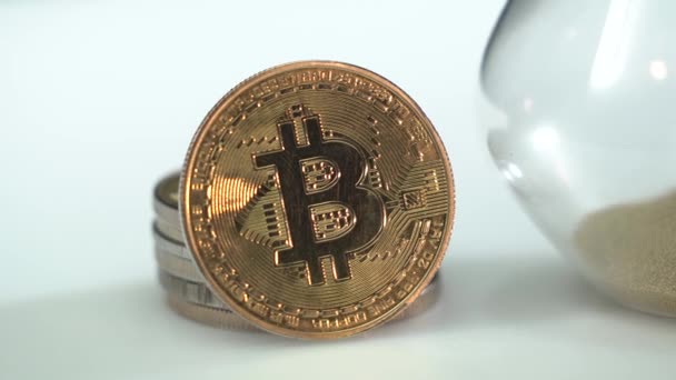 Χρυσό cryptocinn Bitcoin και κλεψύδρα με κίτρινη άμμο σταθεί δίπλα στο λευκό τραπέζι. Ο χρόνος εξαντλείται. Μακρο. Ψηφιακή τεχνολογία μπλοκαρίσματος αλυσίδας. Χρήματα του μέλλοντος — Αρχείο Βίντεο