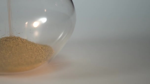 Bottom of hourglass. Yellow sand fallind down. Slow panorama. Extreme close up of a transparent hourglass with flowing sand - time concept. Shot of a sand clock measuring time while the sand is — Stock Video