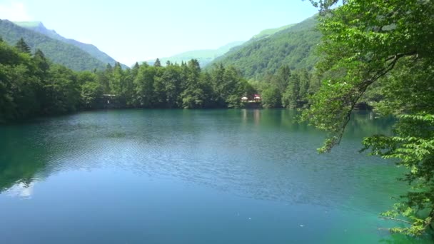 Hermoso lago azul con agua cristalina. Una vista impresionante. Un lago en medio de un bosque verde. Montañas altas detrás de árboles. Panorama horizontal lento. Pequeñas olas en la superficie del agua. — Vídeos de Stock