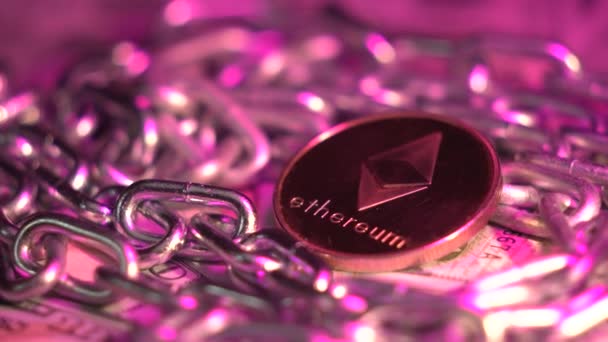 Нова криптовалюта Etherium ETH обертається на столі зі срібним ланцюгом як концепцією технології блокчейн. Рожеве чудове світло відбиває це. Золота монета. Видобуток криптовалюти. Нові цифрові гроші — стокове відео