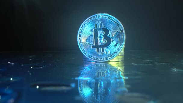 Cryptocoin bitcoin στην γυάλινη επιφάνεια με αντανάκλαση. Πτώση τρέχει κάτω από ένα νόμισμα. Τεχνολογία μπλοκαρίσματος αλυσίδας. Χρήματα στο μέλλον. Νίον και κίτρινο αντανακλούν το νόμισμα. Έννοια επιχειρηματικού εμπορίου — Αρχείο Βίντεο