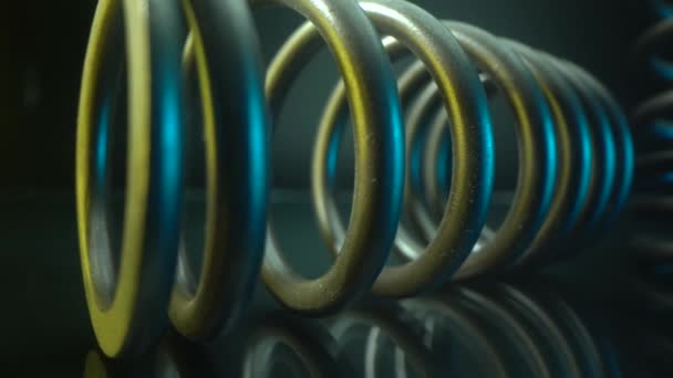 Car spring lies on the glass table with beautiful reflection on the surface. Blue and yellow light on it. Auto part in macro. 3D graphic. Close up with panorama. — Stock Video