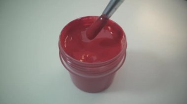 El boyacısının boyasını plastik boya kutusuna ahşap sopayla karıştırması. Kapatın. Kırmızı boya. Pucture 'ı çiz. Beyaz yüzey. Dönen boya ve püskül.