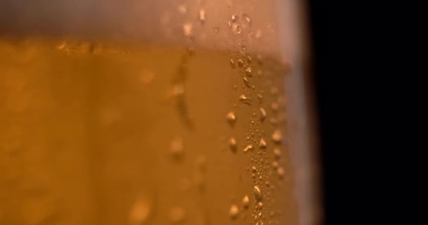 Fresh beer and bubbling foam spilling from glass cup in slow motion on black background. Flass with alcohol rotates on the surface. drops and beer foam on a glass — Stock Video