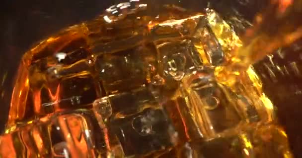 ウイスキー・ブルボンはマクロ・ショットの近くに落下するガラスのスローモーション・アイスに注ぎ込んだ。スローモーションのマクロアイスチューブでウィスキーをグラスに入れるショット — ストック動画