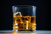 Whiskey töltött egy pohár jég, lassított felvételű, makró lövés, egy fa asztal és sötét háttér. Koncepció: alkohol, szeszes italok, egy jó estéért az alkohol károsítja az egészséget
