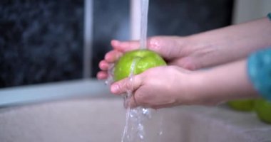 Elma ve elma dilimlerinin üzerine su sıçrıyor kadınların elleri musluktan gelen saf suyla elma yıkıyor. Meyve kabuğunda akan su temizleme kimyasalı. 4k video