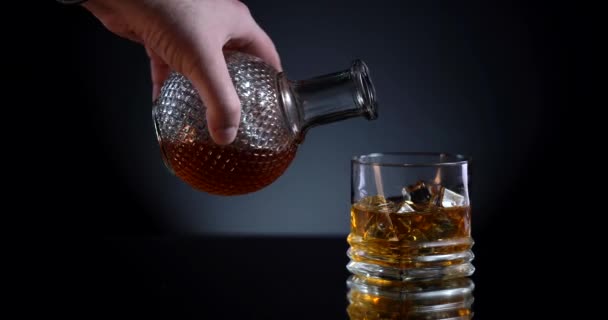 Złota whisky wlewająca się do szklanki z butelki. Z kostkami lodu. Człowiek bierze karafkę i wlewa drogi elitarny alkohol do szklanki. Czarne tło — Wideo stockowe