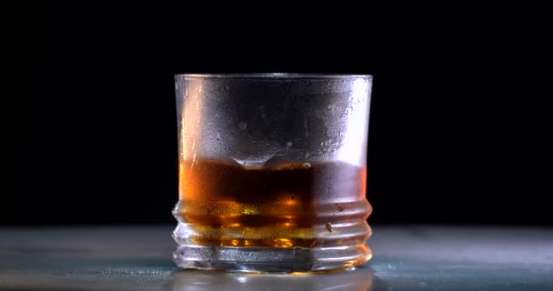 Cantinero Lanza hielo y whisky vertido en un vaso con hielo sobre un fondo de mesa de madera gris. vista frontal. Fondo negro. Concepto de alcohol — Vídeo de stock