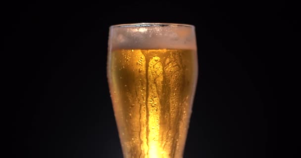 Copo de cerveja fresca fria com espuma e garrafa. Baixo ângulo de espuma branca macia subindo e derramando de copo de vidro de cerveja fria no fundo preto. Gire o copo com álcool saboroso — Vídeo de Stock