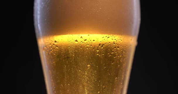 Cold beer with drops, white foam and bubbles. Fresh cold alcohol in pub. Dark background. Low angle shot of golden glass — Stock Video