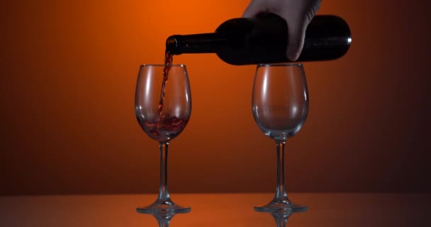 ワインだ。暗めの背景の上にワイングラスに瓶の首から注ぐ赤ワイン。瓶から注ぐ赤ワイン。4kビデオ。オレンジの背景 — ストック動画