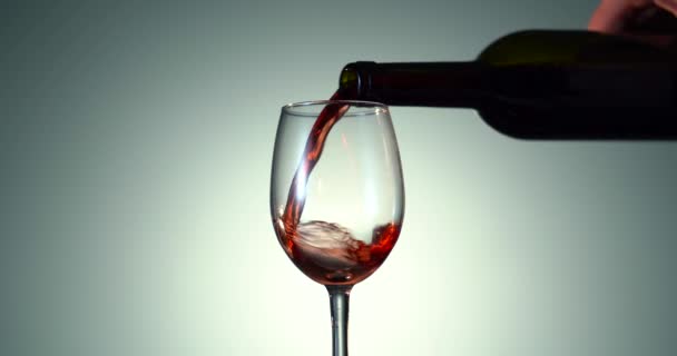 Anggur. Anggur merah menuangkan dari leher botol dalam gelas anggur di atas latar belakang gelap. Anggur mawar mengalir dari botol. Video 4k. Latar belakang putih — Stok Video