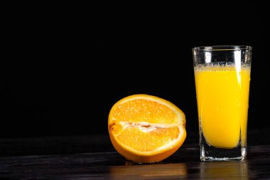 Olgun bir portakal dilimi ve ahşap arka planda uzun bir bardak meyve suyu. Yakın plan. Sağlıklı bir yaşam tarzı. Sağlıklı yemek. Vitaminler. Yaz havası. Tasarım işareti için