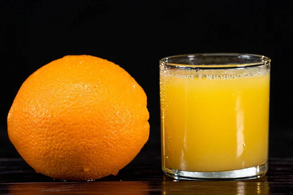 Uma laranja madura e um copo de suco em um fundo de madeira. close-up. estilo de vida saudável. alimentação saudável. vitaminas — Fotografia de Stock