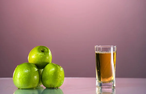 Ein Glas Apfelsaft mit grünen Äpfeln im schönen rosa Hintergrund. Reflektierte Oberfläche. Sommertag. Gute Stimmung. Stockfoto