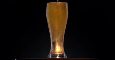 Siyah arka planda hafif biralı bir cam devir. Bardakta bira sallanıyor, kabarcıklar ve köpük yükseliyor. Bir bardak bira saat yönünde döner..