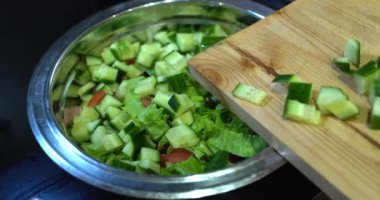 Bir kız yakın plan planında dilimlenmiş sebzeleri salataya koyar. Salata. Yaz. sağlıklı yiyecekler