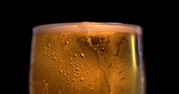 Rotatie van Glas met licht bier op een zwarte achtergrond. Bier zwaait in het glas, bellen en schuim stijgen. Glas bier draait langzaam met de klok mee. — Stockvideo