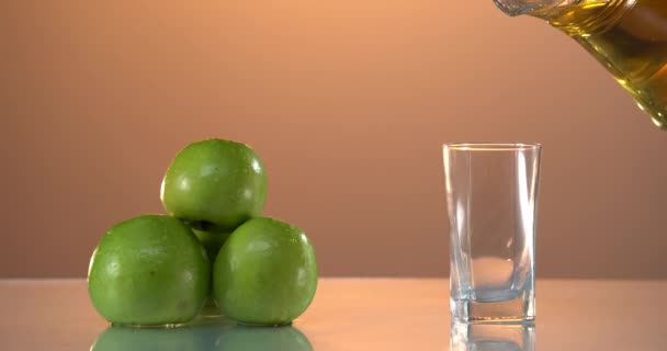 Appelsap in glas op de witte tafel Het maken van vers sap. Langzame beweging gedetailleerde opname van het gieten van heerlijke appelsap in een transparant glas tegen witte achtergrond. Sluit maar af. Gezond voedsel — Stockvideo