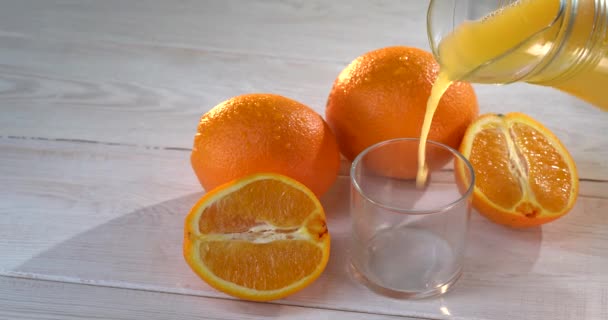El jugo de naranja se vierte en un vaso. hay naranjas frescas en la mesa cercana — Vídeos de Stock